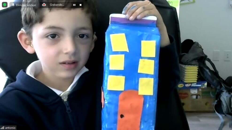 Niño presentando su casa de cartón azul con ventanas amarillas durante la clase en vivo de Eco Craft Makers