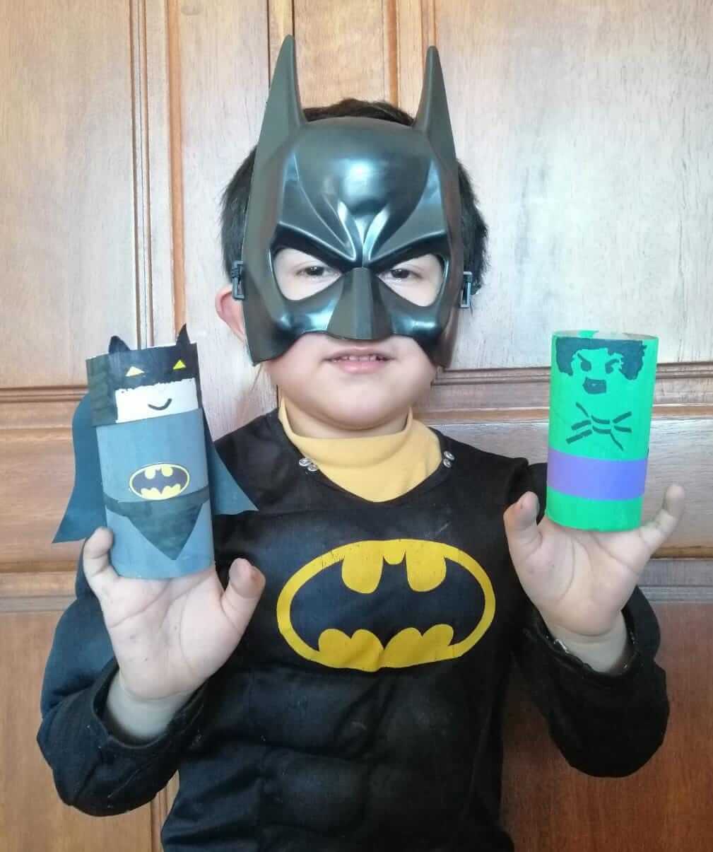 Niño disfrazado de Batman mostrando sus personajes hechos con tubos de cartón reciclado: Batman y el Hulk